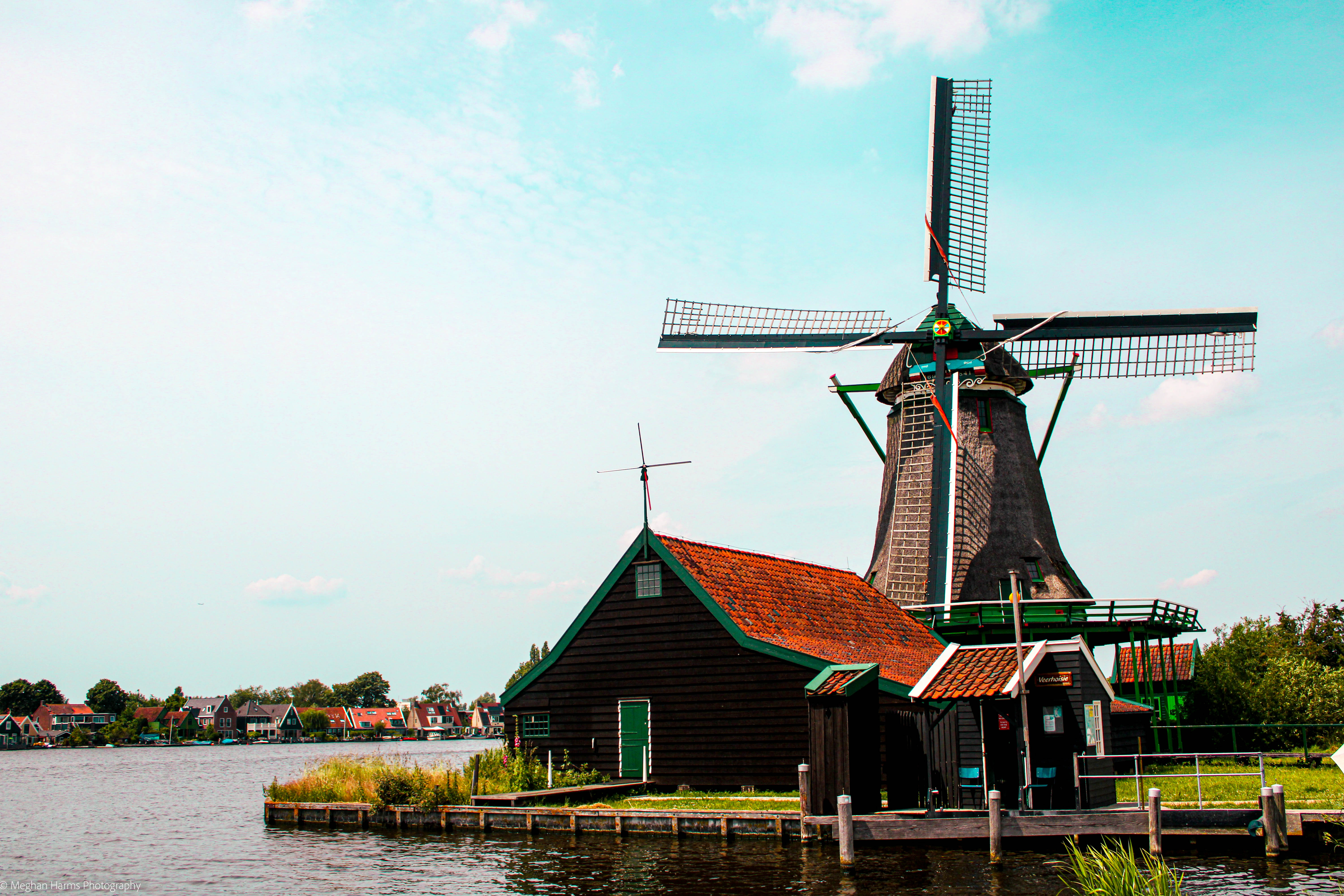 Windmill next to a red roof and brown shingle barn sitting on a lake